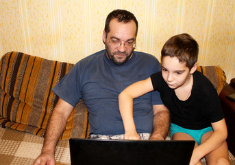 Dad and son are learning to work at the computer. 