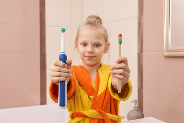 Young girl choice toothbrush. Bamboo or electric tooth brush. Morning dental care routine. Bathroom oral procedure. Both at hands