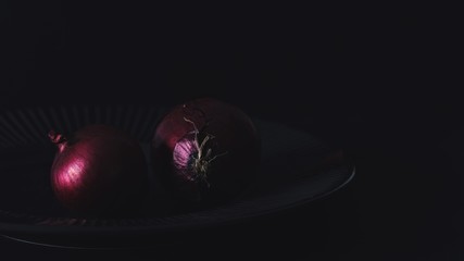 Low key photography of red onions on a plate still life photography