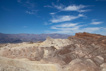 Fototapeta na wymiar Panoramic view of Zabriskie Point, Death Valley National park, with arid rocks in the foreground and mountains in the background under a blue sky