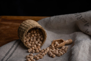 Close-up of basket lying with raw chickpeas on gray linen cloth, wooden table and black background in horizontal with copy space