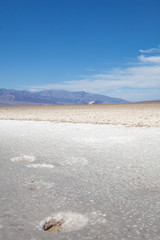 Badwater Basin, lowest point below the sea level in America, in the Death Valley National Park, with a natural hole in the foreground, mountains in the background