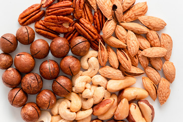 Close shot of assorted brown nuts on a gray background. Macadami, cashews, chopped almonds, pecans healthy food