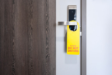 Do not disturb room label tag hotel sign hanging on modern metal doorknob handle on wooden door with workspace for your own writing and design