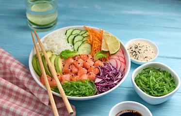 Hawaii salmon poke, rice, seaweed, tomato, cucumber, radish, carrot salad bowl. Home made vegetarian poke. Seafood tasty diet concept. Asian salmon poke bowl on white wood background.