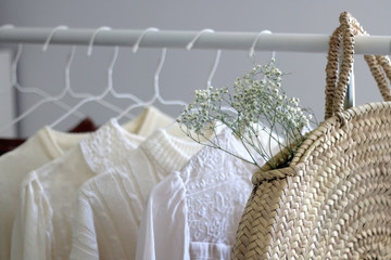 Capsule wardrobe in white and neutral colors and fashionable straw bag. Selective focus.