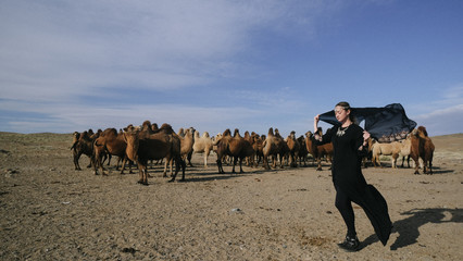 beautiful woman national eastern clothes black color,veil,hijab,abaya ornament her head,portrait steppes camels,strong wind,desert,wildlife,well,decoration,caucasian,slow ,sun