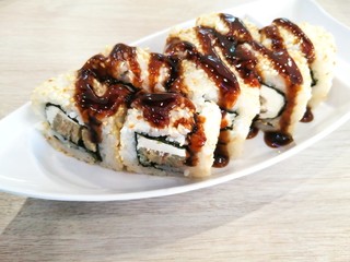 A portion of delicious rolls , sprinkled with sesame seeds and drizzled with teriyaki sauce. Rolls on a beautiful dish in the shape of a boat.