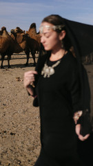 beautiful woman national eastern clothes black color,veil,hijab,abaya ornament her head,portrait steppes camels,strong wind,desert,wildlife,well,decoration,caucasian,slow ,sun