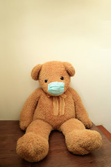 Big brown bear with green hygienic mask sit alone on floor wuth white wall, Sick concept.