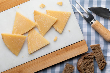 Cured sheep cheese. Cut into pieces on white marble and bread. Fork and knife for cheese. Top View.