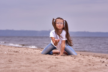 Fototapeta na wymiar Portrait of a teenage girl in glasses and a white T-shirt walking on a sandy shore on a cloudy autumn day.