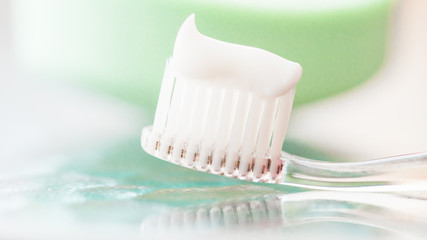 Fototapeta na wymiar Plastic toothbrush with white toothpaste on a glass table and green soap background