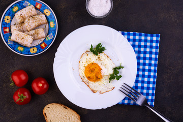 Fried egg with parsley leaves on a white plate. Dark background. View from above.