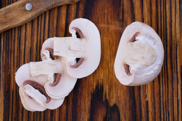 Several slices of fresh champignon mushrooms on a wooden cutting board.
