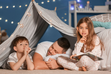 Sleeping father and his little children showing silence gesture at home