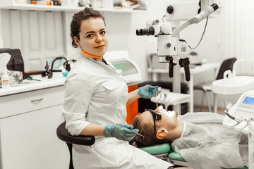 Dentist young woman treats a patient a man. The doctor uses disposable gloves, a mask and a hat. The dentist works in the patient's mouth, uses a professional tool.