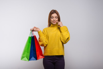 Smiling young woman with shopping bags. Beautiful thoughtful young woman holding colorful paper bags and looking down. Shopping concept
