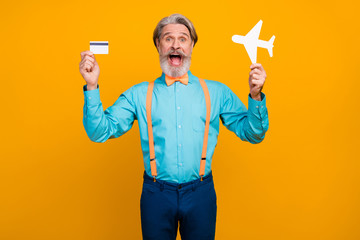Photo of cool grandpa hold paper air plane recommend online buying tickets use plastic credit card wear blue shirt suspenders bow tie pants isolated yellow color background