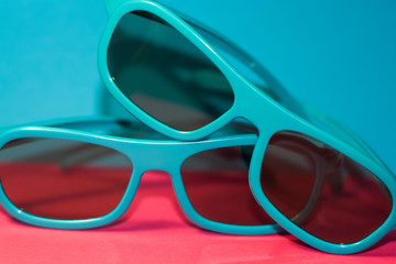 On bright pink background lie sunglasses in plastic blue frame with dark glasses. Summer. Accessories.