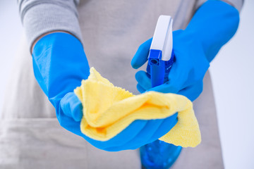 Young woman housekeeper is doing cleaning white table in apron with blue gloves, spray cleaner, wet yellow rag, close up, copy space, blank design concept.