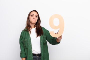 young pretty woman sad, depressed, unhappy, holding a number 9.