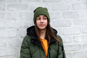 Portrait of a beautiful surprised girl in a yellow sweater and khaki hat, which stands near a white brick wall. The concept of emotions.