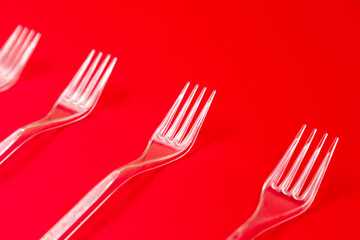Close-up of clear plastic fork on a red background. Disposable tableware pattern