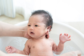 Newborn is being bathed by her mother using tub at home.