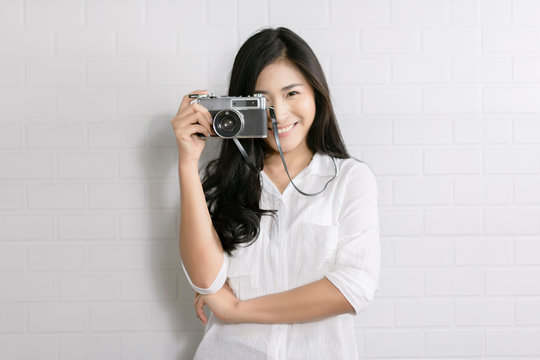 Young Asian woman model with retro film camera wearing a white shirt, long hair indoor over white wall brick background
