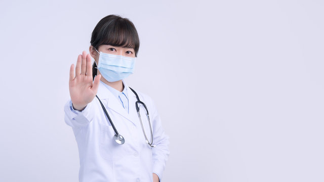 Young Female Doctor Woman Wearing Mask, Making Stop Sign Gesture, Saying No Isolated On White Background, Refusing Virus Disease, Close Up, Blank.