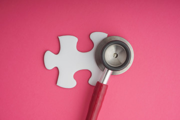 Stethoscope and white jigsaw puzzle on pink background. Cancer awareness campaign concept. Copy space