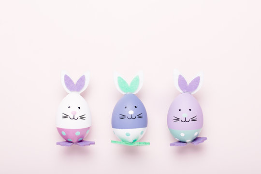 Funny cute bunny eggs in pastel colors on pink table top, Easter holiday concept. Easter decoration for kids flat lay, copy space