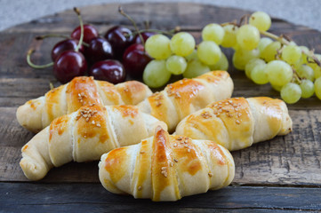 Serbian pastry rolls (kiflice) with sesam on the top and cherries and grapes in background, on the wooden board, close up
