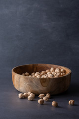 Top view of wooden bowl with chickpeas on dark gray background in vertical with copy space