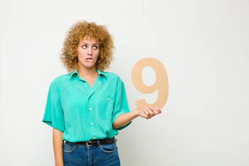 young pretty afro woman surprised, shocked, amazed, holding a number 9.