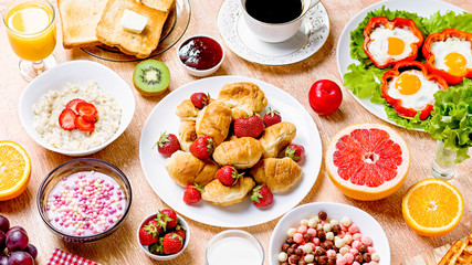 Continental breakfast with cereal, fried eggs, croissants, fruits and drinks on textured table, copy space. Table top with various healthy snacks and foods on rustic background