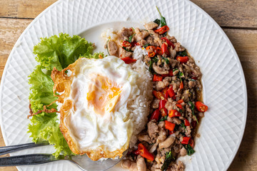 Stir fried minced pork basil with steamed rice and fried egg on a white plate.