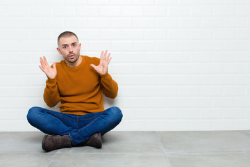 young handsome man looking shocked and astonished, with jaw dropped in surprise when realizing...