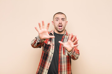 young handsome man feeling terrified, backing off and screaming in horror and panic, reacting to a...