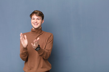 young blonde man feeling happy and successful, smiling and clapping hands, saying congratulations...