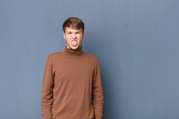 young blonde man feeling disgusted and irritated, sticking tongue out, disliking something nasty...