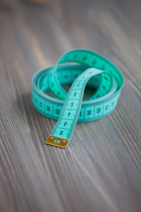 Sewing accessories – the green centimetric measuring tape, tailor tape on a wooden background