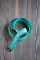 Sewing accessories – the green centimetric measuring tape, tailor tape on a wooden background