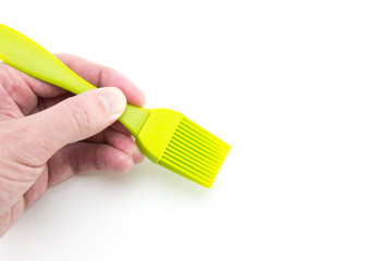 The kitchen brush is silicone, light green in the hand of a person with light skin. Plastic accessories for the kitchen, cooking and coating. White isolated background.