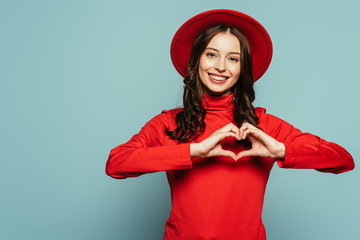 happy stylish girl showing heart symbol with hands on blue background