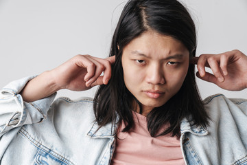 Fototapeta premium Image of displeased asian man looking at camera and plugging his ears