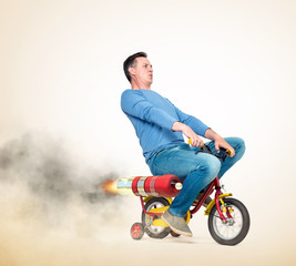 Cool man in casual wear rides a children's bike with alternative rocket engine. On a light yellow background. - obrazy, fototapety, plakaty