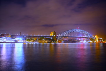 Sydney Harbour Bridge illuminating the harbour and circular quay with vibrant colourful lights at midnight in NSW Australia