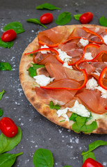 Colourful Italian pizza with prosciutto ham, pepper and decorated with tomato and basil